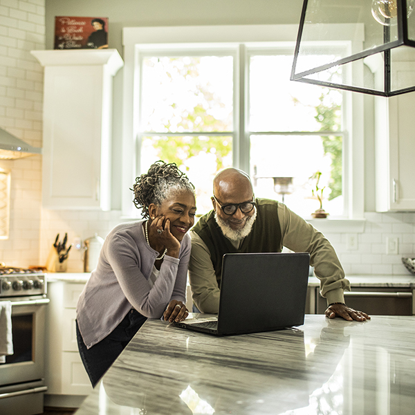 Senior couple using laptop in kitchen of suburban home